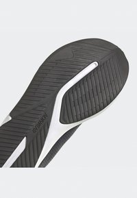 Suola di scarpe da ginnastica nera in gomma testurizzata, con un accento bianco curvo e scanalature flessibili per aderenza e supporto.