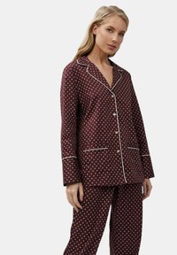 Set di pigiami color mogano con pois bianchi, dotato di colletto a punta, chiusura con bottoni e piping bianco su polsini e tasche. Tessuto morbido.