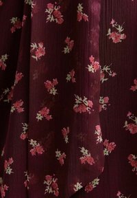 Tela burdeos con un aspecto texturizado, adornada con patrones florales en rosa y blanco. Diseño ligero y con caída.