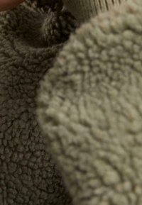 Gros plan d'un tissu polaire texturé marron et beige montrant des fibres douces, duveteuses et bouclées à la lumière naturelle.