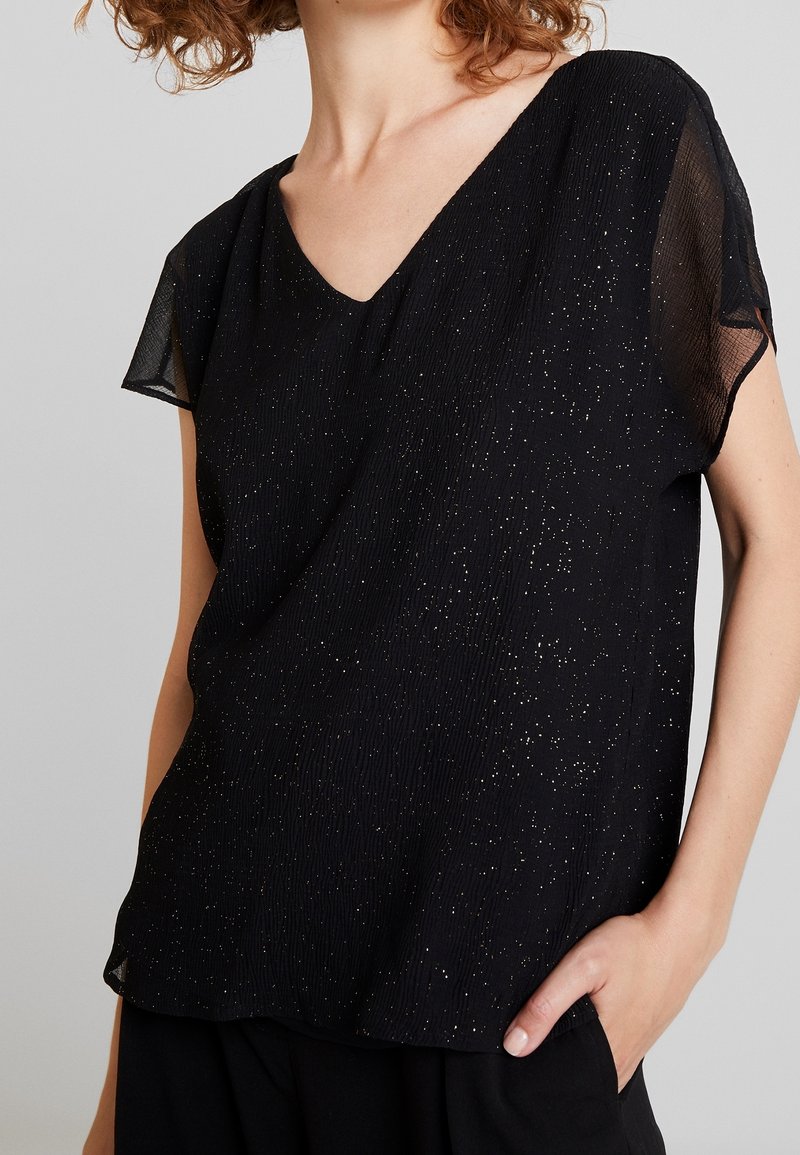 Black short-sleeve top with a V-neck, featuring a textured fabric with gold speckles and a relaxed fit. Accented with sheer sleeves.