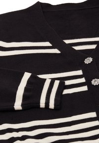 Cárdigan negro con rayas horizontales blancas, puños acanalados y escote en V. Presenta botones decorativos en forma de flor. Textura de punto suave.