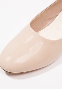 Chaussure plate en cuir verni beige avec un bout arrondi et une texture lisse. Intérieur doublé de tissu doux, dotée de caractéristiques de design minimalistes.
