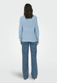 Mėlynas megztinis su tekstūruotu raštu, turintis laisvą siluetą ir kritusiomis pečių siūlėmis, derinamas su šviesiais džinsiniais plačiais kelniais.