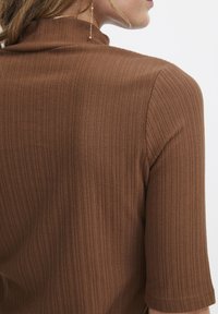 Brown ribbed top with a high neckline and short sleeves, featuring a textured fabric. No visible patterns or accents.