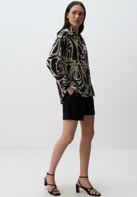 Camicia a maniche lunghe a motivo bianco e nero, abbinata a pantaloni corti neri. La camicia presenta design astratti e polsini abbottonati.