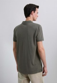 Camisa polo verde oliva de manga corta, con cuello acanalado y aberturas laterales en el dobladillo, hecha de un tejido texturizado.