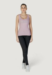 Top a maniche lunghe ribattuto viola con logo "GUESS", abbinato a jeans neri e sneakers bianche. Design semplice e aderente, con spalline larghe.