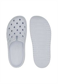 Witte rubberen schuifsandalen hebben een gegolfd ontwerp met ronde gaten voor ventilatie. De structuur van de zool zorgt voor grip en stabiliteit.
