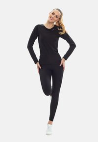 Black long-sleeve athletic top paired with black leggings and white sneakers. The fabric appears lightweight with a smooth texture.