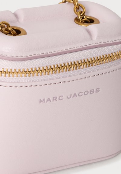 Γωνία τσάντας Marc Jacobs σε ανοιχτό ροζ χρώμα με χρυσά ιμάντες αλυσίδας, χρυστό φερμουάρ και ορατό όνομα εμπορικής επωνυμίας σε λείο δερμάτινο φόντο.