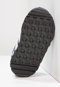 Svart gummiskosula med ett hexagonalt mönster och "adidas"-logotypen tydligt präglad. Kanterna har en texturerad yta.