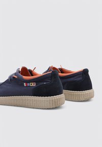 Zapatos de ante azul marino con forro naranja, puntera redondeada y suela de goma texturizada en beige. Presentan coloridos acentos bordados en el costado.