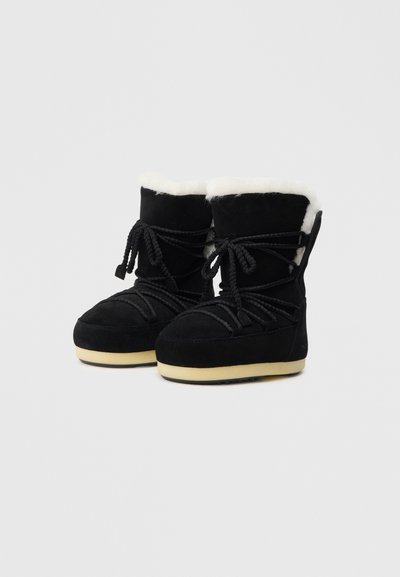 Bottes d'hiver en daim noir avec doublure en fausse fourrure blanche, bout rond et semelle en caoutchouc texturé ; dotées de doubles lacets noirs.