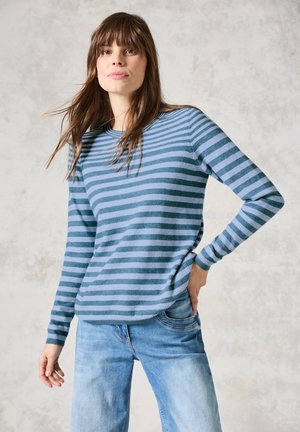Pull à manches longues rayé bleu et vert en tissu doux, associé à un jean bleu clair. Il présente un col rond et une coupe décontractée.