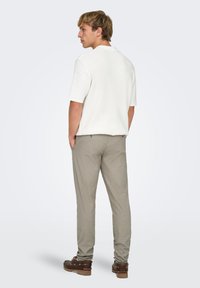 Polo blanc à manches courtes avec un tissu texturé, associé à un pantalon gris clair et des chaussures brunes, vu de dos.