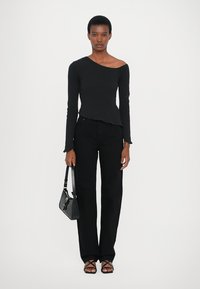 Maglietta nera a maniche lunghe con scollatura asimmetrica, abbinata a pantaloni neri a gamba larga e sandali neri con laccetti. Una piccola borsa nera completa il look.