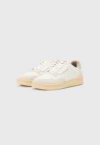 White sneakers with a beige rubber sole, featuring a blend of leather and suede textures, perforations on the toe, and tonal accents.