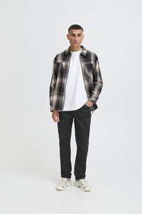 Kostkovaná košile v černé, šedé a krémové barvě přes bílé tričko, doplněná černými kalhotami a krémovými teniskami. Moderní střih s propracovanými detaily.