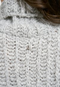 Hellgrauer Strickpullover mit einem strukturierten Stichmuster und einem kleinen silbernen Knopfdetail am Kragen.
