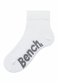 Calcetín de algodón blanco hasta el tobillo con un logo gris "Bench." en el lateral. Presenta un puño acanalado y una textura suave.