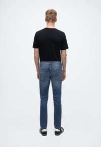 Černé tričko s krátkým rukávem, modré džíny s kapsami na zadní straně, rovné nohavice a světle modrá barva, nošené s černo-bílými teniskami.