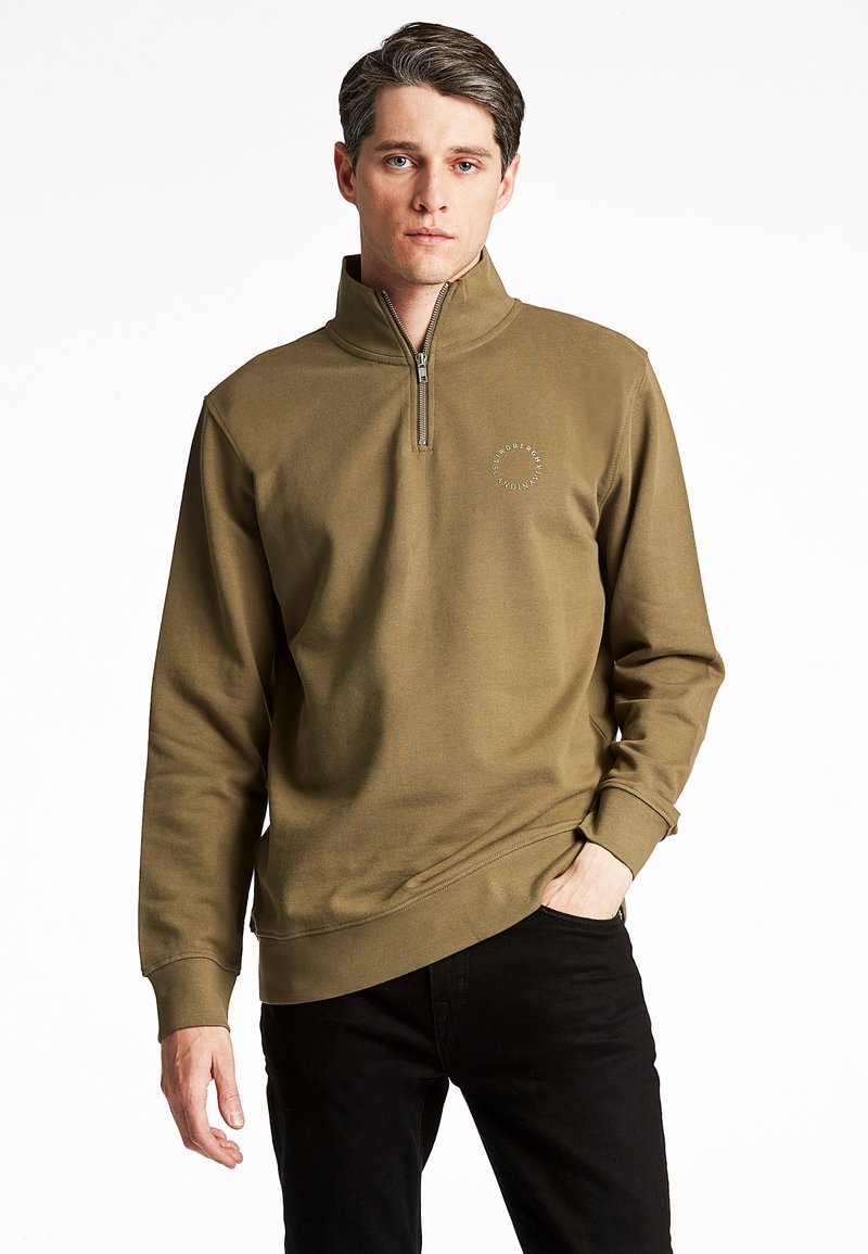 Felpa verde oliva con zip a quarto, polsini a coste e logo decorativo sul petto. Tessuto morbido, vestibilità comoda, abbinata a pantaloni neri.