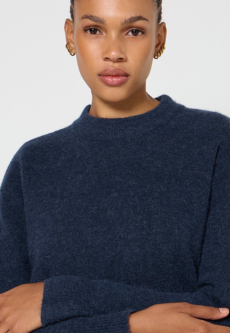 Dunkelblauer gestrickter Pullover mit hohem Ausschnitt, aus weichem, texturiertem Material, mit langen Ärmeln und lässiger Passform.