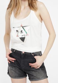 Top bianco senza maniche con una stampa geometrica che presenta palme; abbinato a pantaloni corti in denim grigio scuro con dettagli strappati e orli arrotolati.