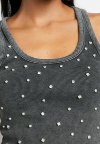 Top tipo tank gris con textura, adornado con embellishments plateados dispersos, y escote redondeado.