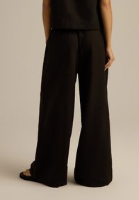 Czarne szerokie spodnie od pasa wykonane z miękkiego materiału, z luźnym krojem i bocznymi kieszeniami, zestawione z prostym krótkim topem.