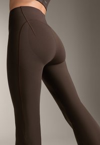 Barna sport leggings, sima, rugalmas anyagból, magas derékkal és kontrasztos varrással az oldalakon.