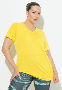 T-shirt giallo a scollo a V in tessuto leggero, con maniche corte e vestibilità rilassata, abbinato a leggings verdi a fantasia con motivi circolari.