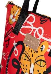 Rode tote bag met een speelse luipaardontwerp, aangevuld met zwarte en witte grafische elementen; gouden logobord voegt een metallic detail toe.
