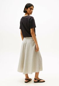T-shirt nero a maniche corte abbinato a una gonna a strisce bianca e beige al ginocchio, insieme a sandali neri flat.