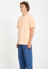 Peachfarvet kortærmet t-shirt med rund hals, parret med løse blå denimbukser med en sidelomme.