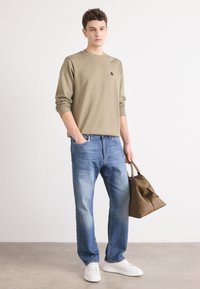 Olive green long-sleeve shirt, faded blue straight-leg jeans, white sneakers, brown leather bag. Simple design with a round neck and logo.