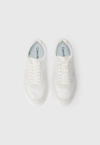 Λευκά αθλητικά παπούτσια με συνδυασμό λείων και υφασμάτινων υλικών, στρογγυλή μύτη, επίπεδα κορδόνια και διακριτικό λογότυπο της μάρκας στη γλώσσα.