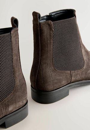 Brūnas potītes zābaki ar strukturētu krokodila rakstu un sieta sānu paneļiem, ar zemu melnu gumijas papēdi un vilkšanas cilpām ērtai uzvilkšanai.