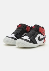 Svart og hvite sneakers med røde detaljer, med en teksturert stoffoverdel, polstret ankelstøtte og en gummisåle med et rutenettmønster.