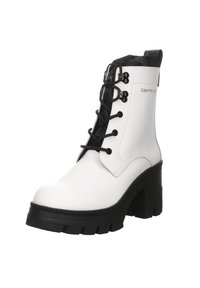 Botín blanco hasta el tobillo con un acabado brillante, cordones negros, suela de plataforma gruesa negra y detalles acolchados en negro en el cuello.