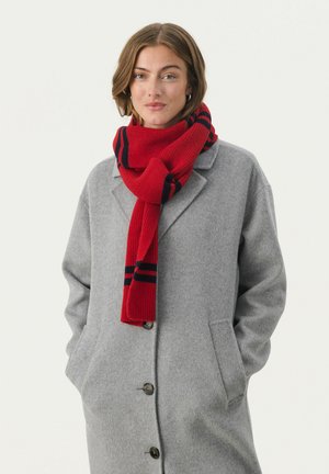 Roter gestrickter Schal mit marineblauen Streifen, um den Hals drapiert, getragen mit einem hellgrauen Wollmantel mit Knopfverschluss und seitlichen Taschen.