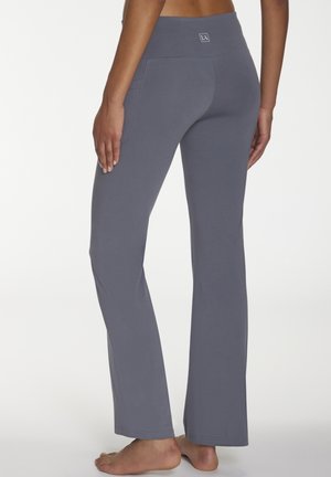 Grau ausgestellte Leggings mit einem breiten Bund, weicher Textur und genähten Nähten. Verfügt über ein Logo auf der Rückseite des Bundes und Seitentaschen.