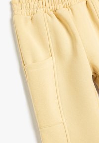 Helle gelbe Jogginghosen mit einem gerafften Bund, seitlichen Taschen und weicher Textur. Zeigen Stoffnähte und glatte Verarbeitung.