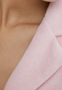 Tessuto rosa chiaro con texture e colletto a revers, che mette in risalto un collo liscio e dettagli delle cuciture, su uno sfondo di tono caldo della pelle.