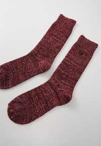 Calcetines de punto en un rico color rojo con una textura moteada, con un puño acanalado y un pequeño detalle del logo en un lado.