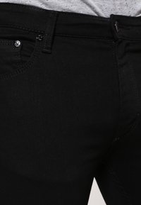 Los jeans de mezclilla negros tienen una textura suave, un corte ajustado y un diseño minimalista con una cremallera frontal y dos bolsillos.