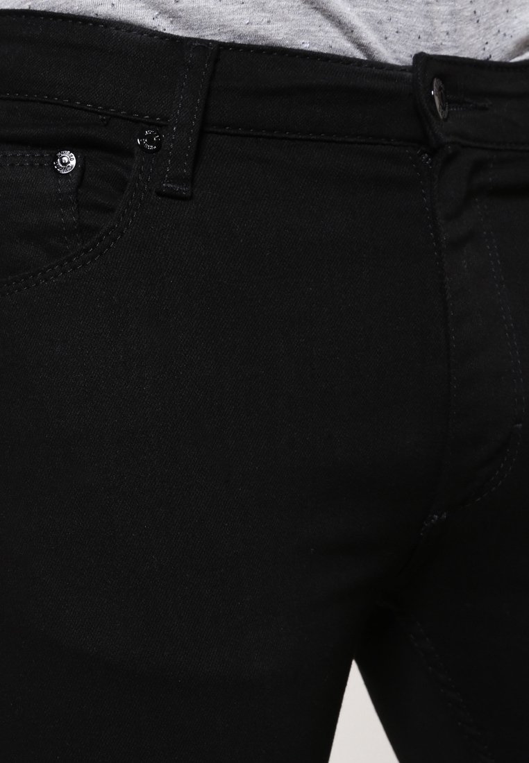 Los jeans de mezclilla negros tienen una textura suave, un corte ajustado y un diseño minimalista con una cremallera frontal y dos bolsillos.