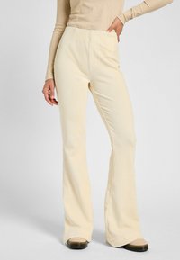 Pantaloni a zampa d'elefante in corduroy color crema con righe verticali, dotati di una vita alta e una finitura liscia. Scarpe con platform nere visibili.