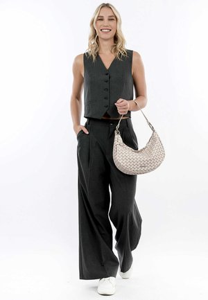 Gilet senza maniche grigio con bottoni frontali, abbinato a pantaloni larghi; tiene in mano una borsa beige con motivo; le sneakers bianche completano il look.